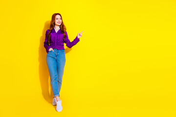 Full body length photo of red hair young woman in purple shirt and jeans looking empty blank space isolated on yellow color background