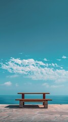 Seaside Bench with Clear Blue Sky. A wooden bench overlooking the ocean with a clear blue sky and scattered clouds, offering a peaceful, scenic view.