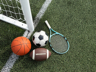 A variety of sports equipment including an american football, a soccer ball, a tennis racket, a tennis ball, and a basketball
