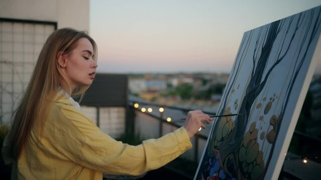 An artist is painting outdoors at sunset, finding creative inspiration in the beautiful scenery. A young woman painting on a rooftop, capturing creativity and inspiration in the golden hour