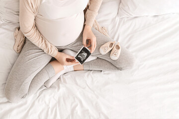 Pregnant woman looking at her baby sonography, enjoying future motherhood with first photo of her...
