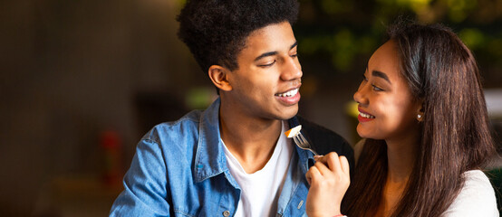 Naklejka premium African American guy and girl are standing close, smiling warmly at each other. They appear happy and engaged in a pleasant conversation, panorama with copy space
