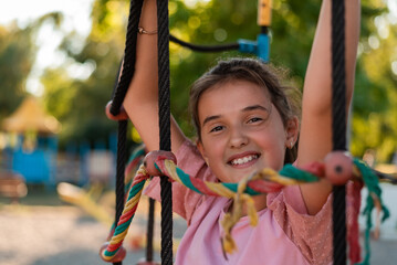 A happy kid girl climbing up on the rope in the park playground.