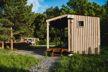 This image captures a rustic wooden cabin nestled in a lush green forest. The peaceful setting, enhanced by clear blue skies and natural sunlight, offers a serene retreat for nature lovers.