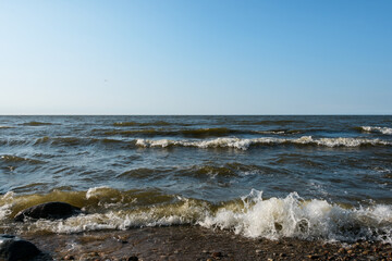 Small foaming sea waves roll onto the shore. Clear sky with barely noticeable cloud haze. Evening side sunlight