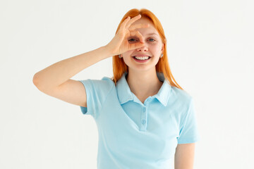 Fototapeta premium Beautiful young woman wearing casual blue t-shirt doing ok gesture with hand smiling, eye looking through fingers with happy face.