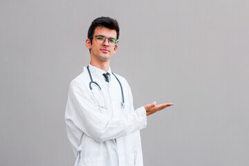 Man portrait of a doctor wearing a white coat and eyeglasses and a stethoscope looking into the camera on a gray background, copy space, space for text, health