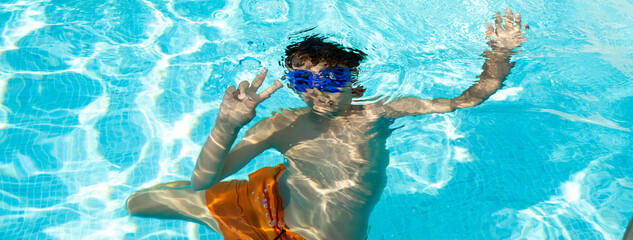 Boy on summer vacation underwater in swimming pool in swimsuit
