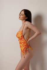 A beautiful slender girl in a orange one-piece swimsuit in a Moroccan-style sand studio. A pretty...