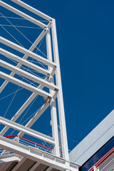 Low-angle view of a modern white steel structure against a clear blue sky, showcasing geometric design and architectural elements in a crisp, high-contrast urban setting.