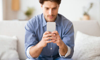 A man sits on a couch indoors, looking intently at his phone.