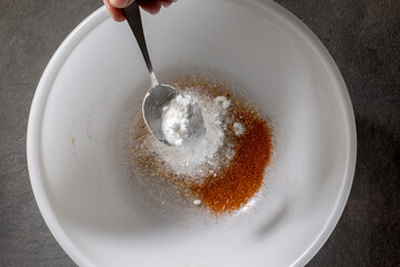 chef add baking powder into a white bowl with a metal spoon, prepares mix of spices for chicken wings. process of making crispy chicken wings