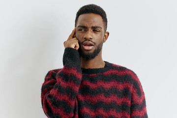 Young african american man attentively listening with hand to ear, wearing a stylish red and black...