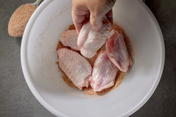 cook put fresh raw chicken wings in bowl of spices