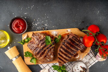 Grilled beef steak on wooden cutting board with ketchup sauce and condiments, top view copy space