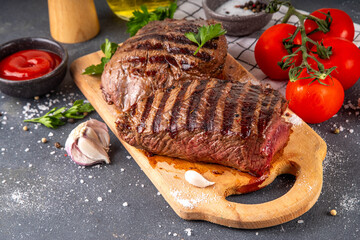 Grilled beef steak on wooden cutting board with ketchup sauce and condiments, top view copy space