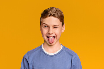 Playful teen boy winking and sticking out tongue, orange studio background