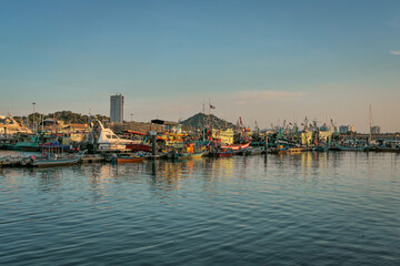 Fototapeta premium A panoramic view of a harbor filled with docked fishing boats, with the setting sun casting a warm glow on the water and boats.