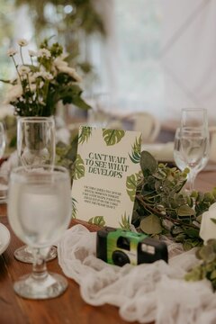 Table setting at a wedding with a disposable camera, flowers, and a sign encouraging guests