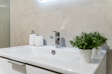modern bathroom design with light-colored tiles, white furniture and a white sink. Green plants on...
