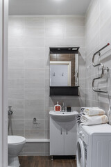 modern bathroom design with light-colored tiles, white furniture and a white toilet bowl. There is a washing machine and a mirror on the bathroom wall.