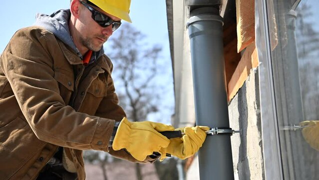 Construction Worker is Installing Gutter Downspout on a House Exterior