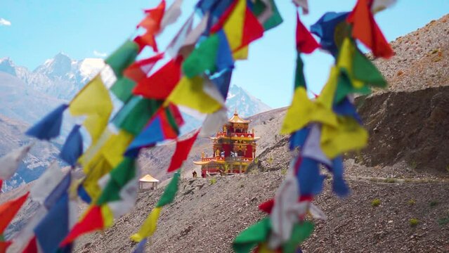 Rack focus shot of Prayer flags in front of Gue Monastery on the way towards Spiti Valley in Himachal Pradesh, India. Focus shifts from prayer flag to the monastery in the back. Religious background.