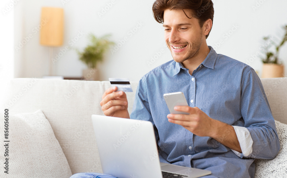 Poster a man sits on a couch, smiling as he makes a payment online using a credit card and smartphone.