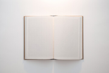 A notebook with a grid pattern on the pages is open on a white surface. The pages are blank, ready for writing or drawing.