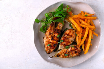 Roasted pink salmon steaks with French fries and arugula served on the plate. Top view