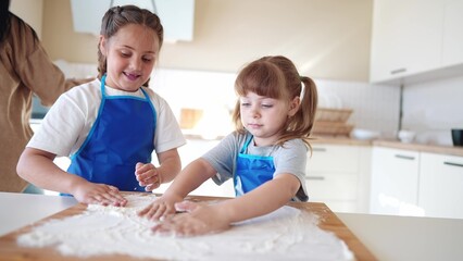 Fototapeta premium children making dough in the kitchen. two little girls cook in the kitchen knead dough and flour indoors. happy family kid dream concept. children play cooking dough together at home fun