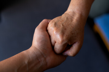 Fototapeta premium Close-up of a mother and her adult son's hands tightly clasped, representing their strong bond, love, and mutual support