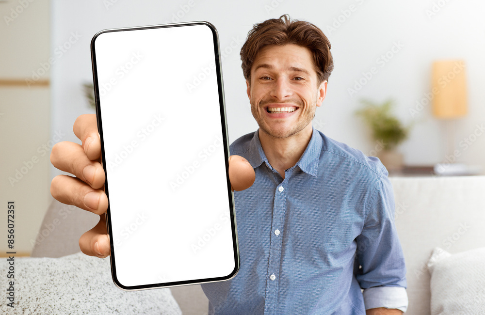 Poster a smiling man holds a smartphone with a blank white screen, looking directly at the camera.