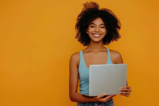 Cheerful young african american business woman with laptop on bright yellow background working standing in profile with copyspace background