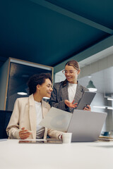 Two smiling business woman work together with documents and use digital tablet at the office