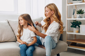 Mother and daughter bonding time as mom gently combs her child's hair on a cozy living room couch