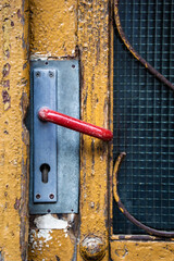 A Weathered Wooden Door With a Red Door Handle and a Wire Mesh Security Screen entry point security concept