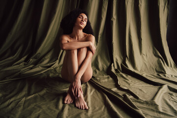 No filter photo of gentle sensual girl sitting floor cuddling loving herself on textile khaki color background