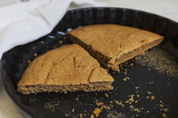 close-up for two remaining slices of a traditional Estonian Barley Scone in a black ceramic baking...