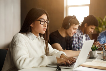 Concentrated international classmates preparing for exams in library with laptops and phones