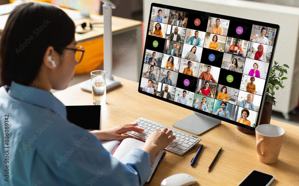Poster a woman wearing earbuds sits at her desk in front of a computer monitor displaying a video conferenc
