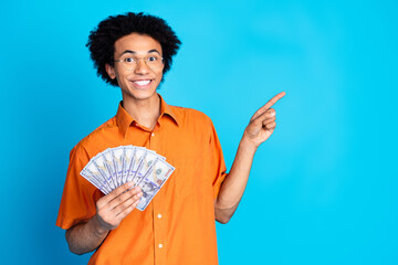 Photo of funky cool guy dressed orange shirt eyeglasses rising money fan pointing emtpy space isolated blue color background