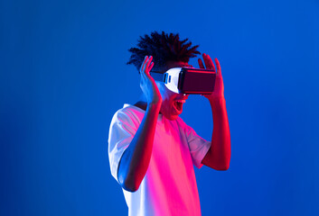 Surprised young African American looking through VR holding interesting object hologram on pink...