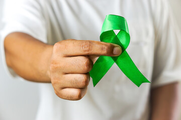 A close-up of a hand holding a green awareness ribbon, symbolizing support and solidarity for various health and social causes.