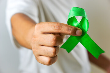 A close-up of a hand holding a green awareness ribbon, symbolizing support and solidarity for various health and social causes.