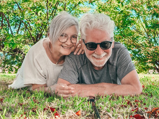 Fototapeta premium Smiling elderly couple while lying in the grass in the park looking towards the camera. Their expressions radiate happiness and freedom, capturing a moment of joy and connection in natural setting