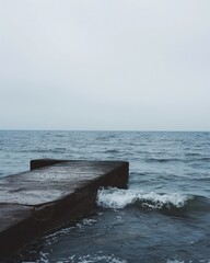 Simple image of a concrete pier jutting into a calm sea with gentle waves hitting the structure