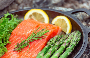 Healthy baked salmon steaks with greens and asparagus in a black cast iron skillet. A delicious low-carb breakfast.