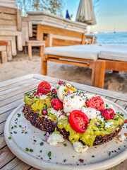 Bruschetta with avocado and cream cheese, decorated with berries and flower and served on a beach