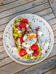 Bruschetta with avocado and cream cheese, decorated with berries and flower and served on a beach